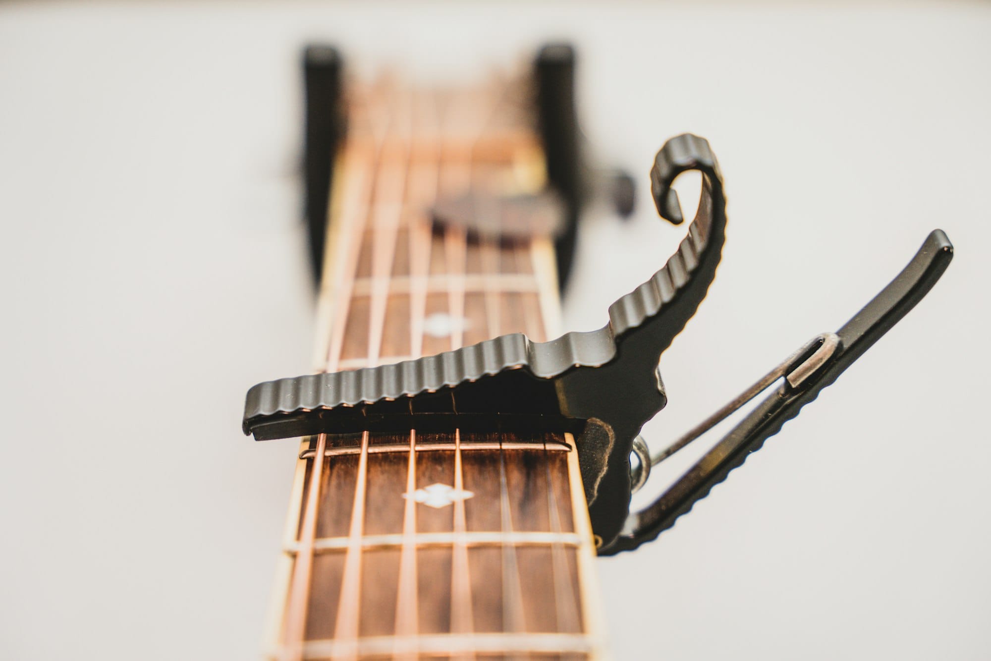 Close up of a guitar capo clamped to the neck of an acoustic guitar.